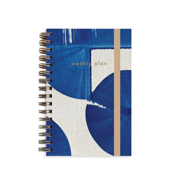 Indigo A6 Weekly Undated Planner notebook by Moglea with a patterned cover and open pages showing weekly layout.